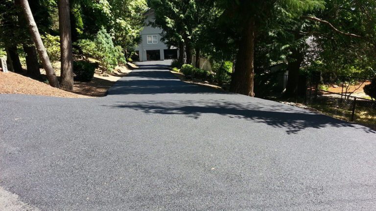 Newly paved driveway leading to a gray home